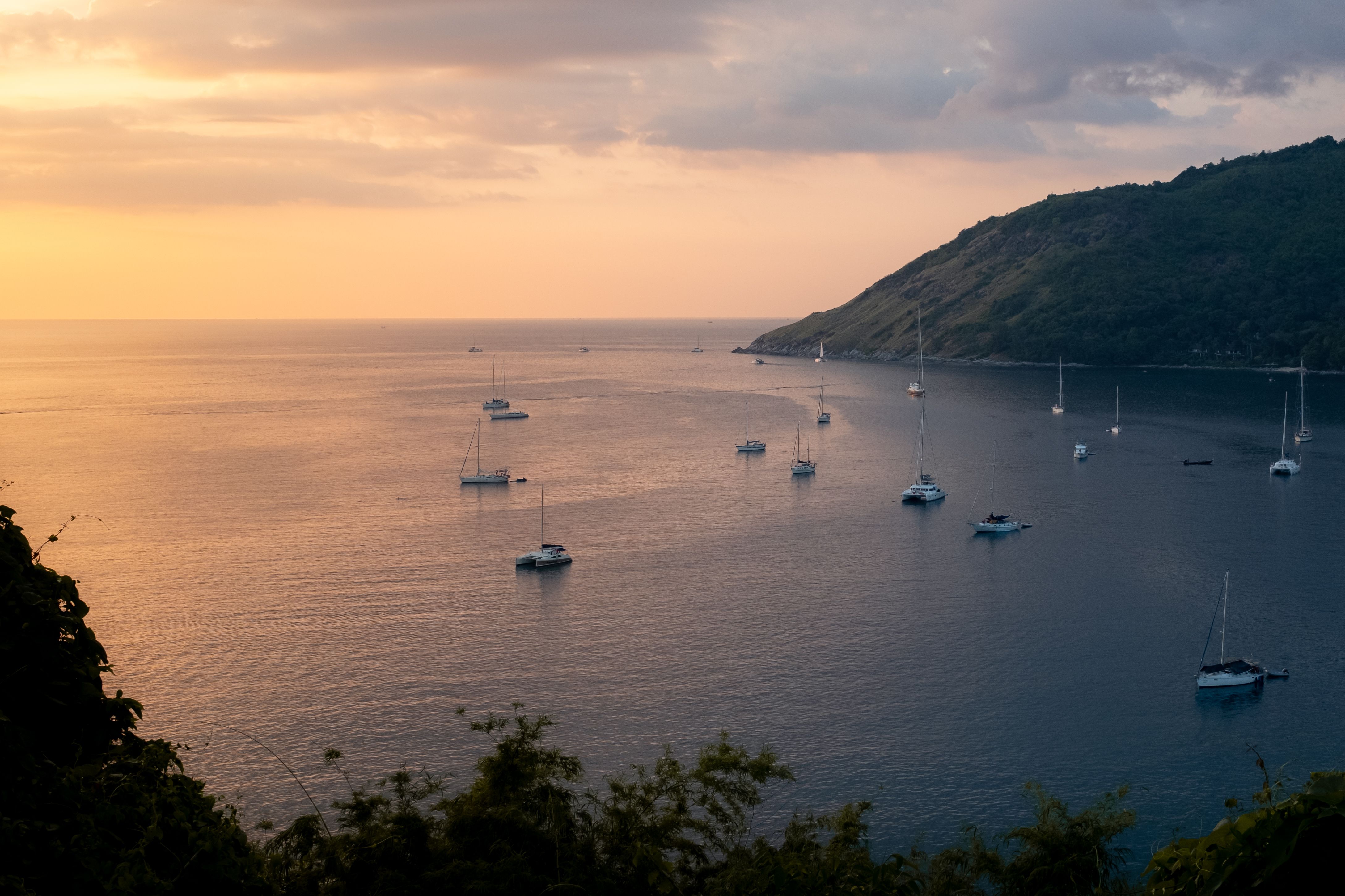 פוקט: Tranquil view of sailboats and yachts in Phuket, Thailand with a warm sunset horizon.