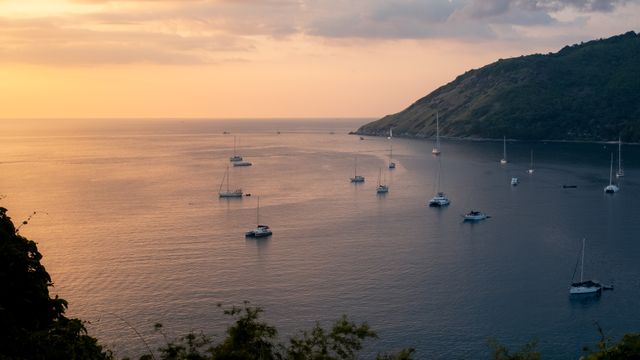 פוקט: Tranquil view of sailboats and yachts in Phuket, Thailand with a warm sunset horizon.