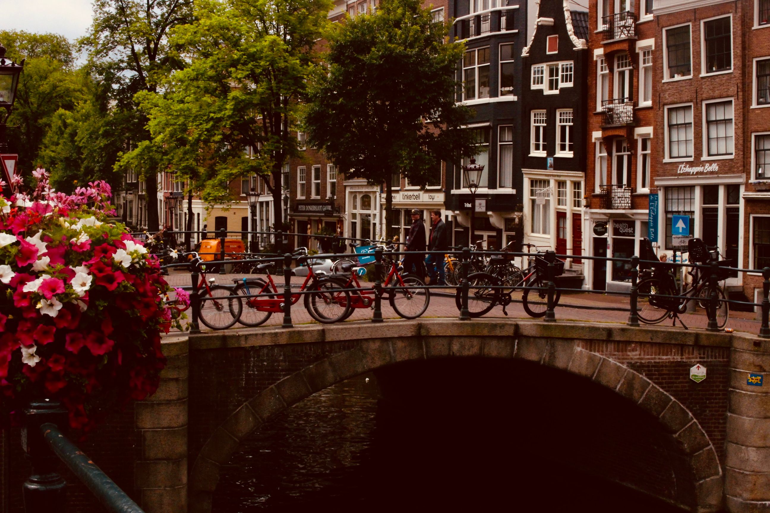 אמסטרדם: Scenic view of an Amsterdam canal bridge adorned with bicycles and vibrant flowers, perfect for urban travel in