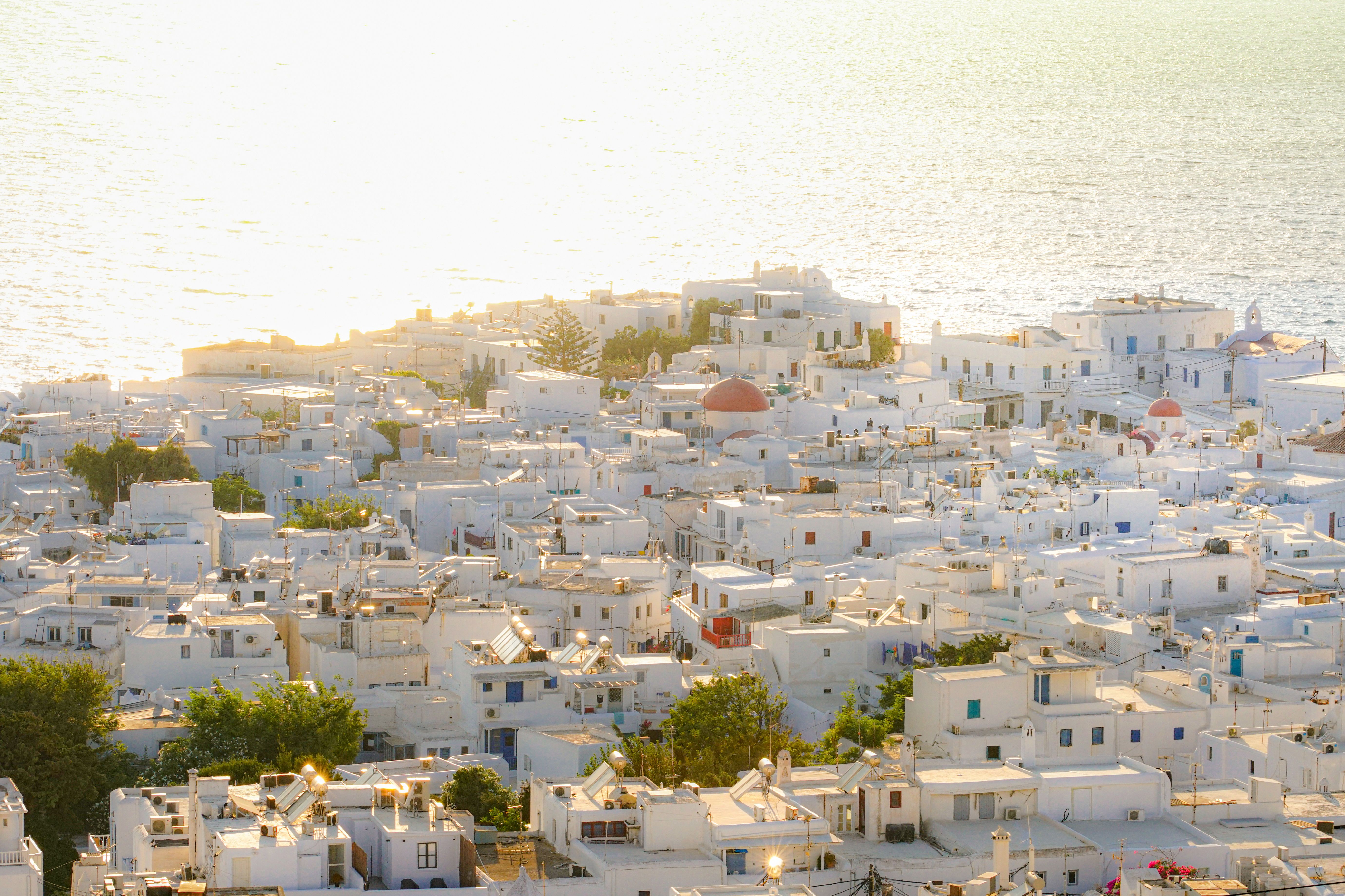 מיקונוס: A picturesque view of Mykonos town with white buildings and sea at sunset.