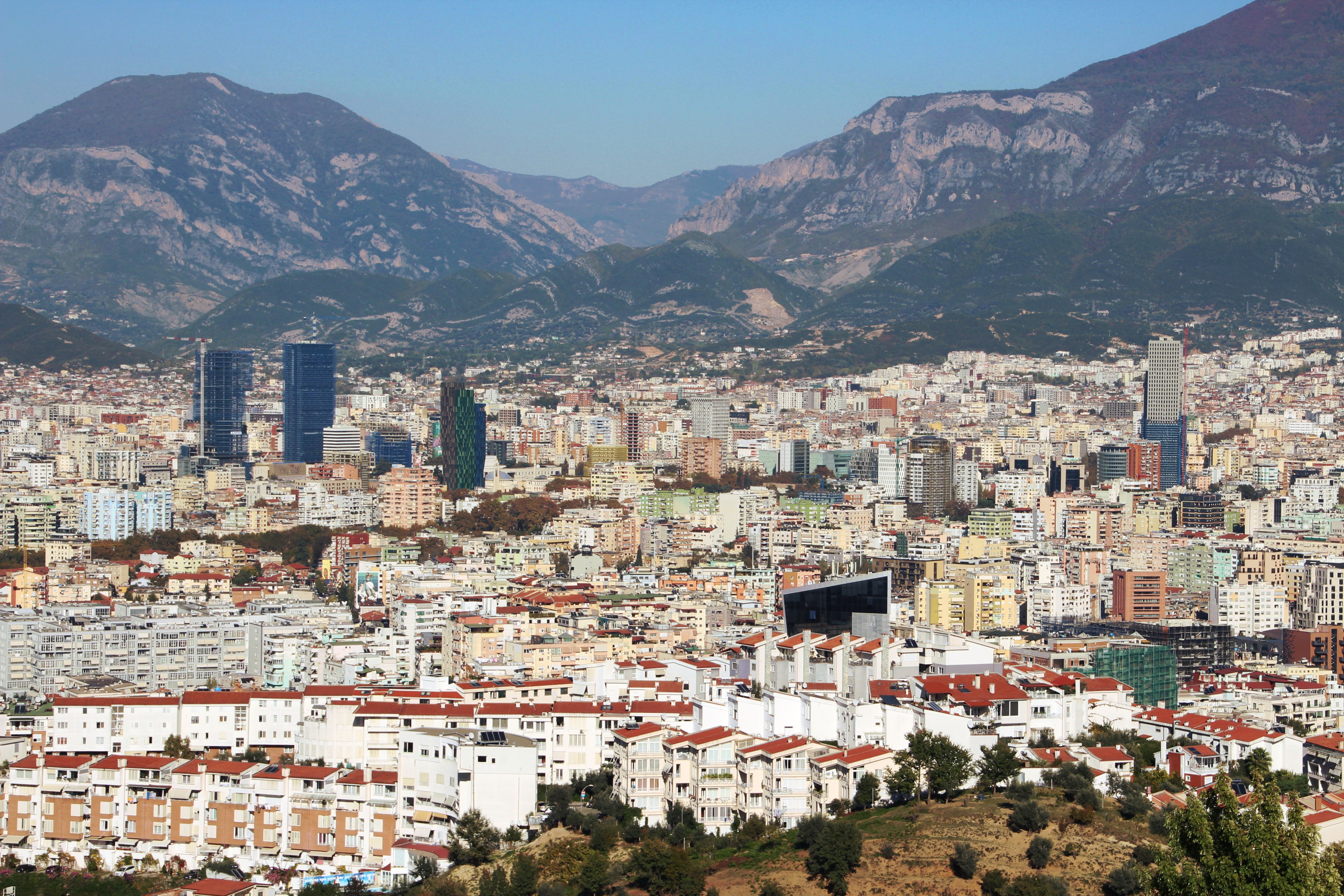 טירנה: Aerial view of Tirana, Albania, featuring urban landscape and distant mountains.