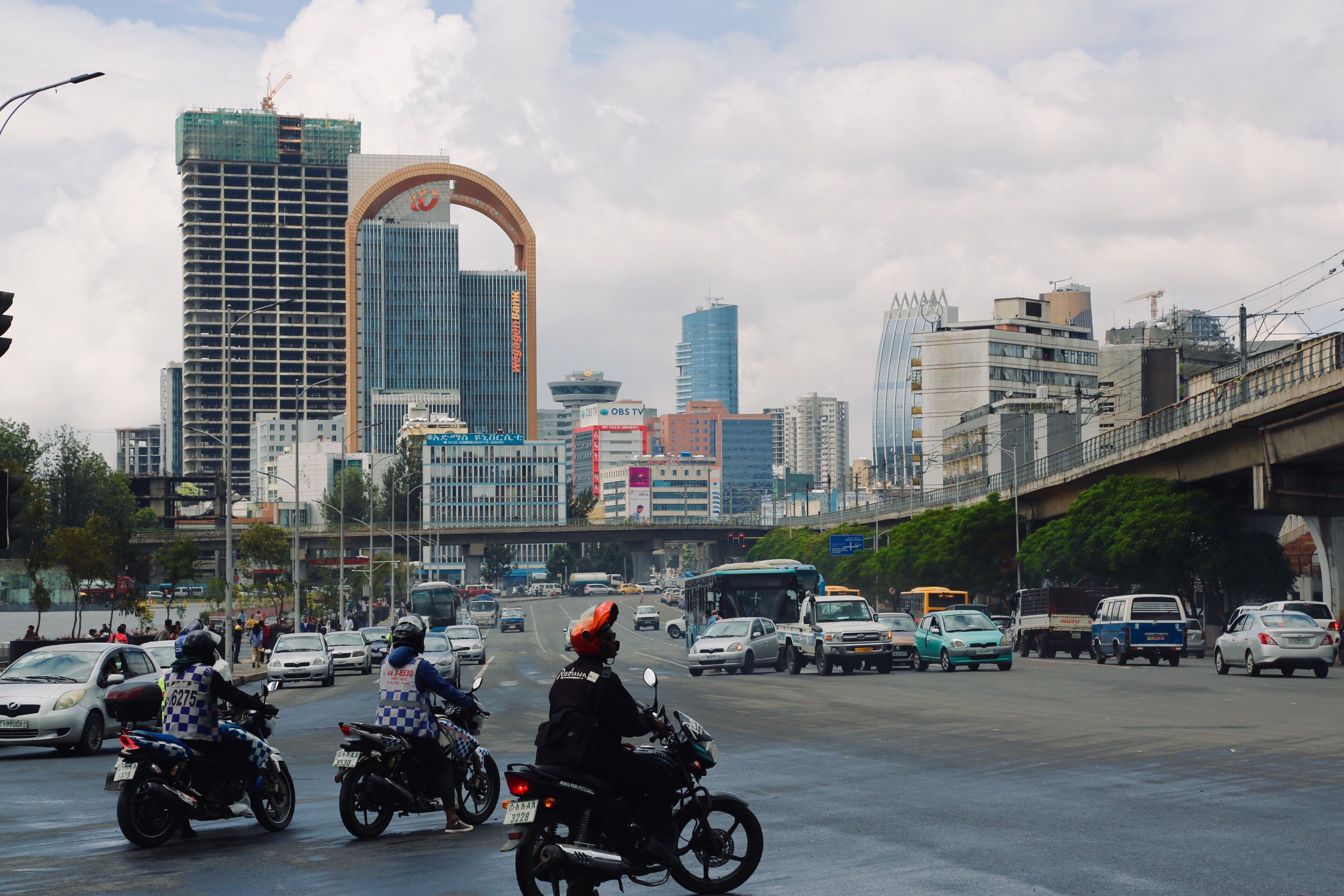 אדיס אבבה: Bikers and cars bustling in Addis Ababa's cityscape with iconic buildings and clear skies.