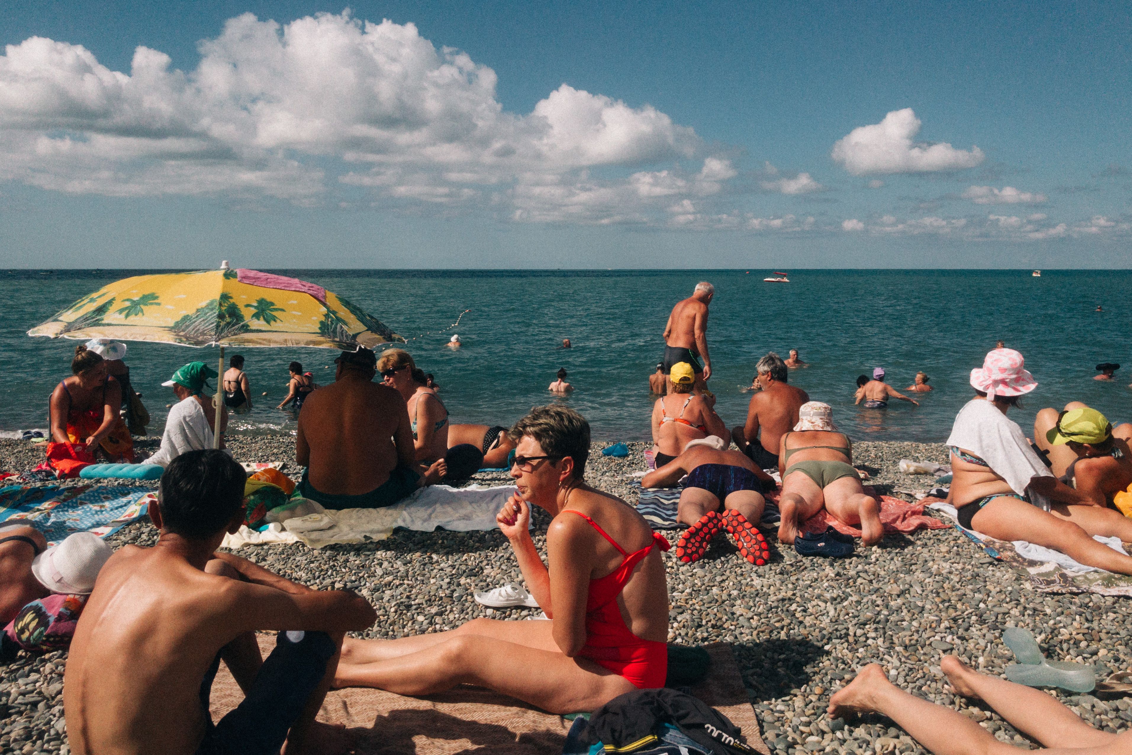 סוצ'י: A vibrant scene of people relaxing and sunbathing on a pebbled beach in Sochi, Russia.