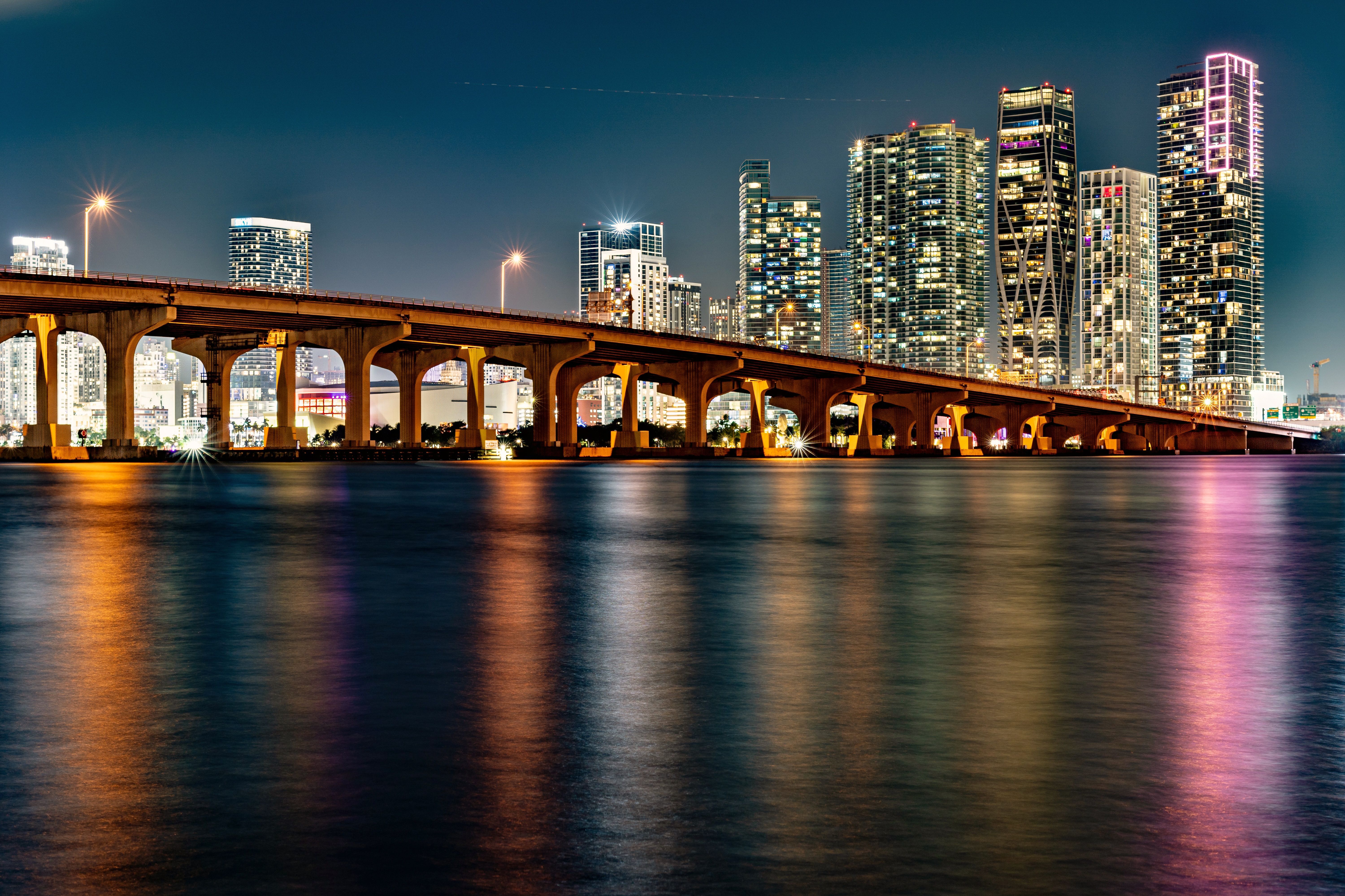מיאמי: Illuminated Miami skyline with a bridge reflection at night.