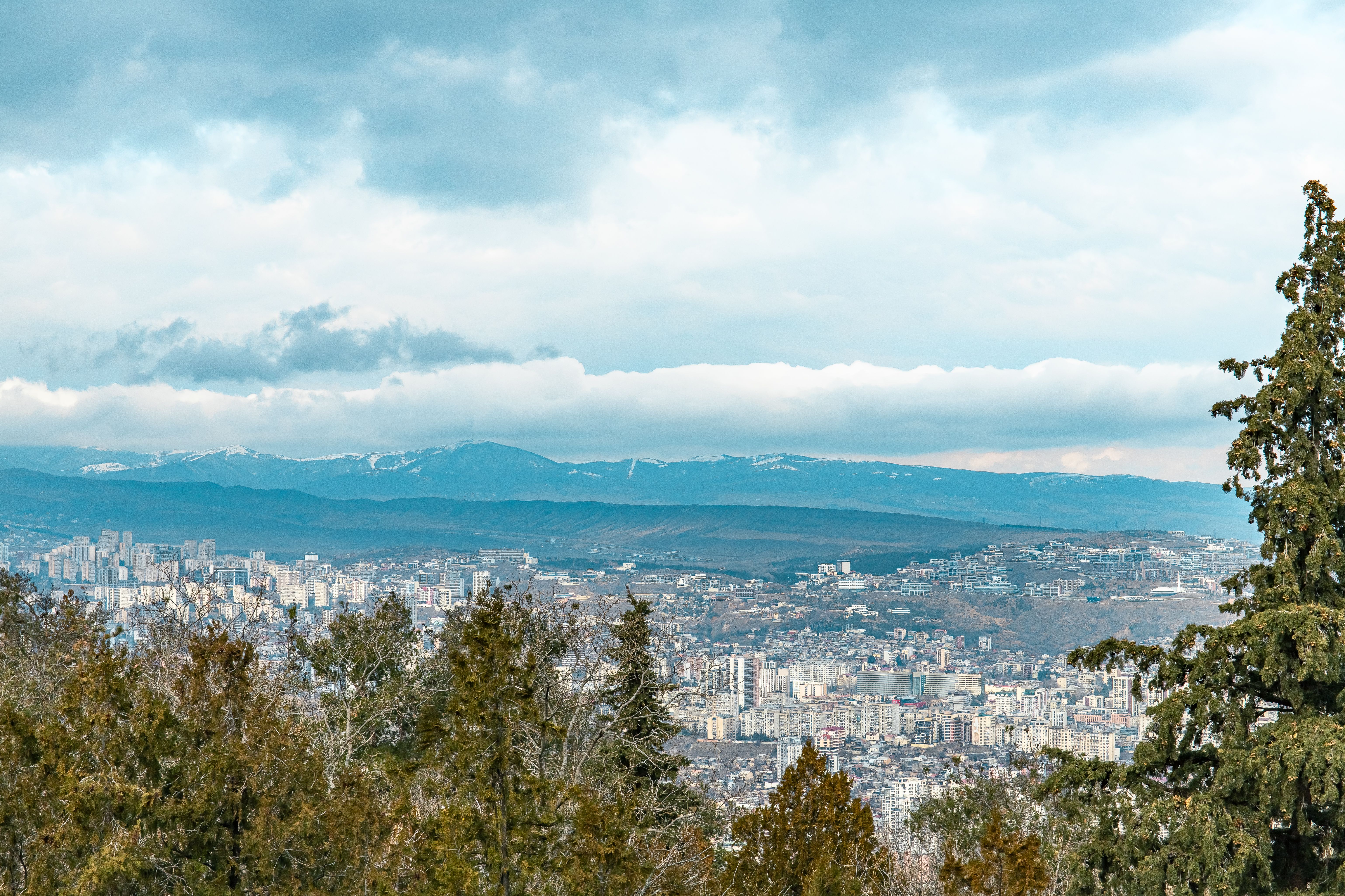 מינרלניה וודי: Aerial view of Tbilisi and surrounding mountains with cloudy skies.