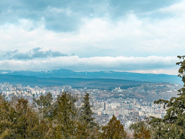 מינרלניה וודי: Aerial view of Tbilisi and surrounding mountains with cloudy skies.