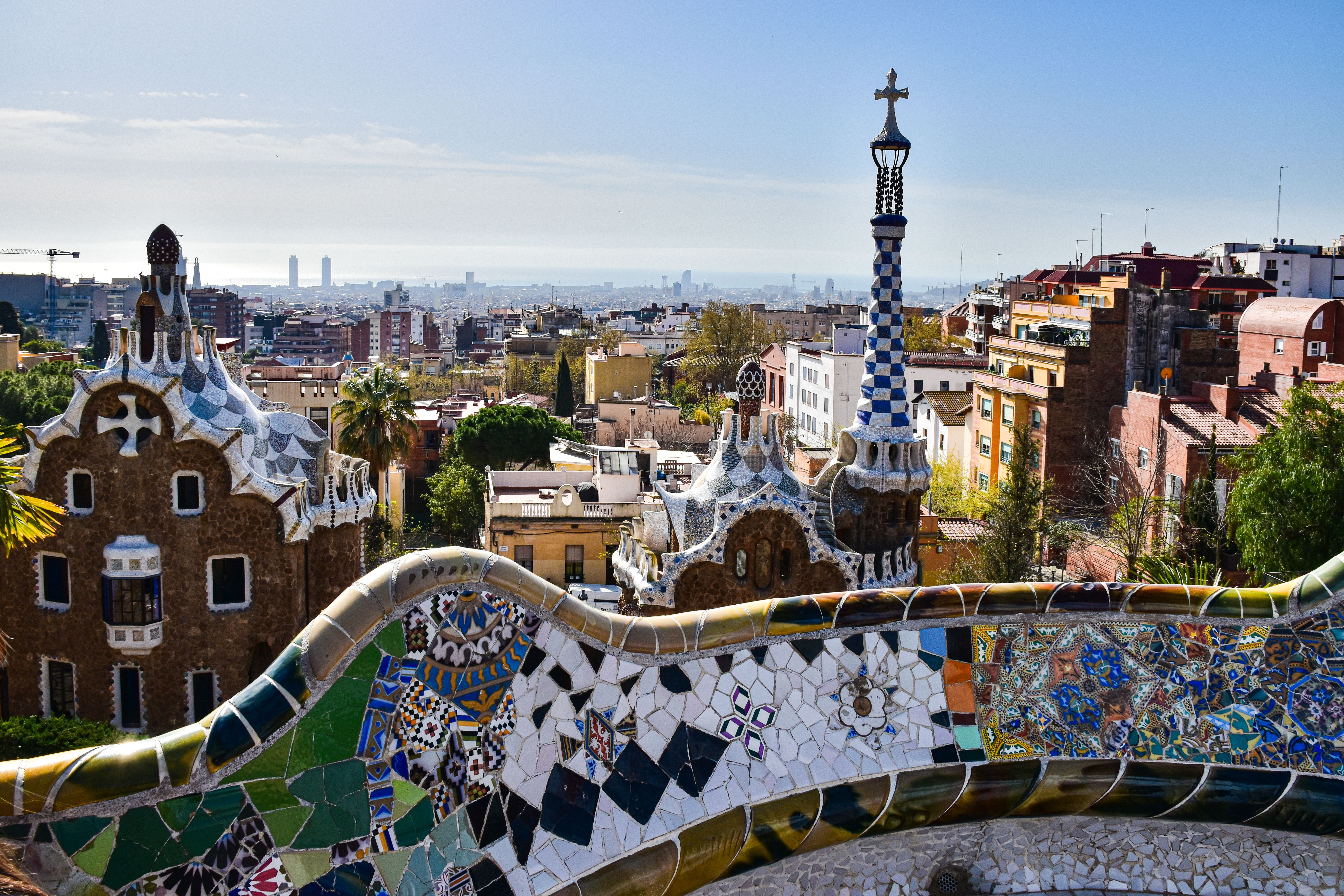 ברצלונה: Gaudí's iconic mosaic architecture in Park Güell with a view of Barcelona's cityscape.