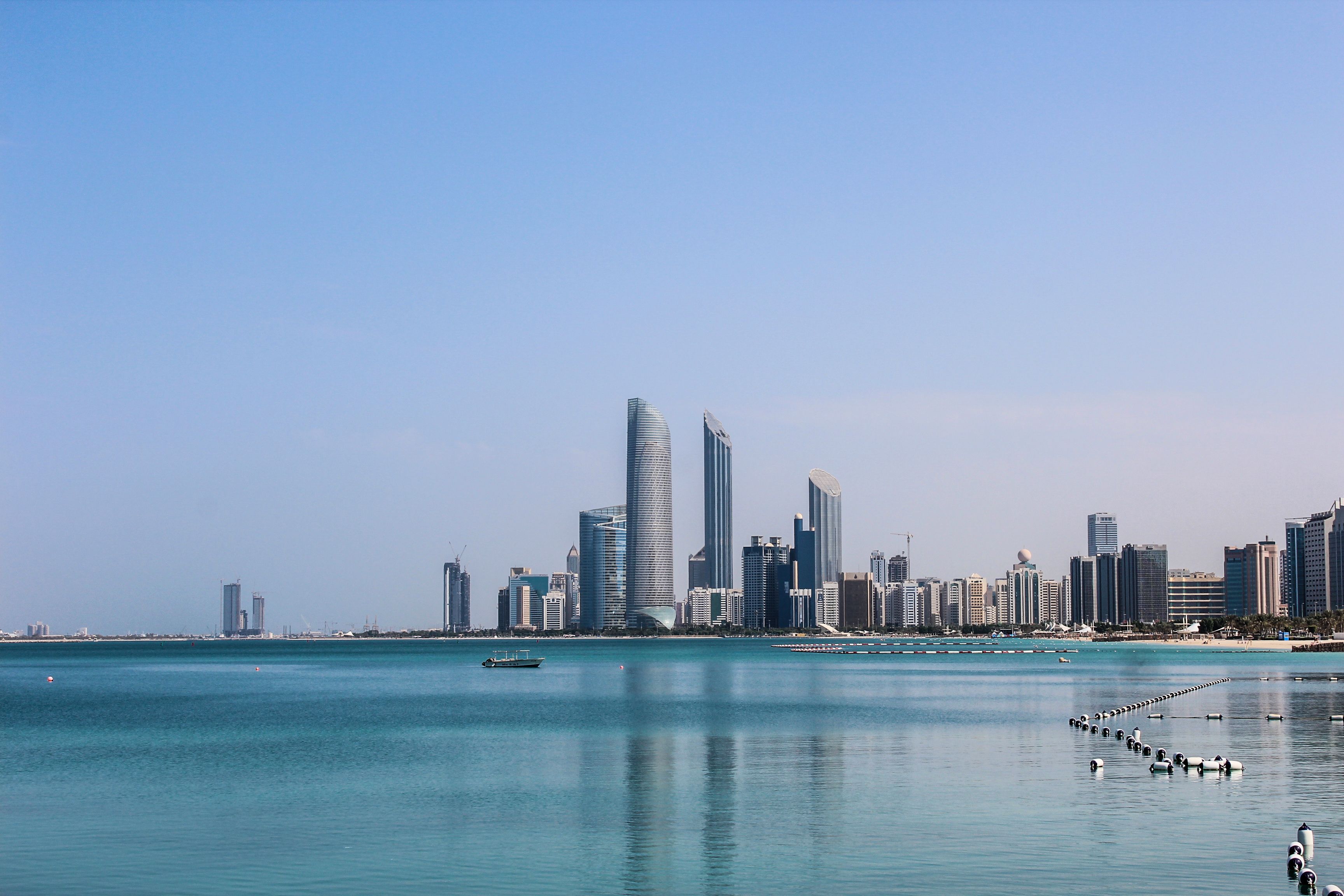 אבו דאבי: Stunning view of the Abu Dhabi skyline reflecting in the calm Gulf waters on a sunny day.