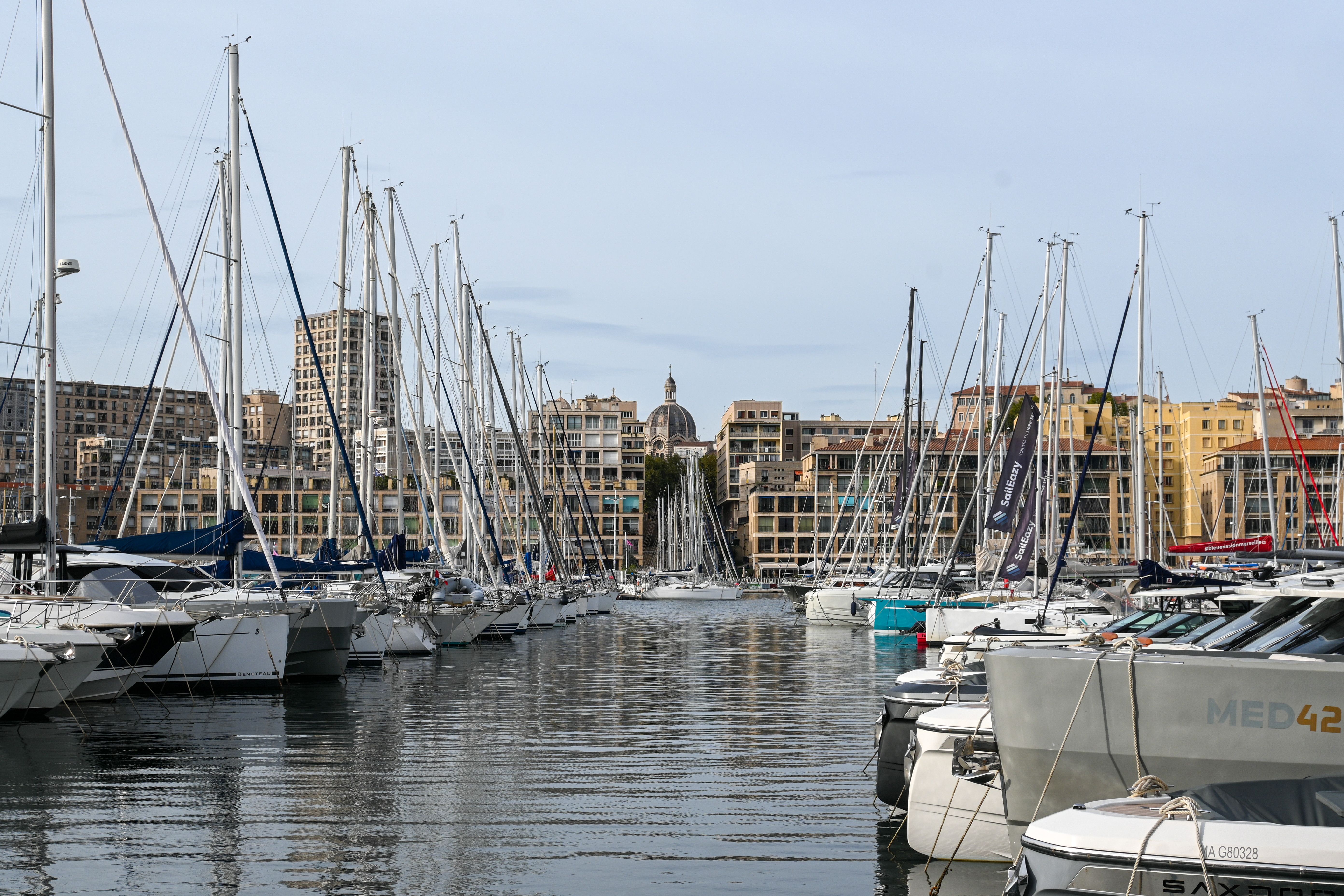 מרסיי: Stunning view of sailboats docked at the Old Port of Marseille with cityscape backdrop.