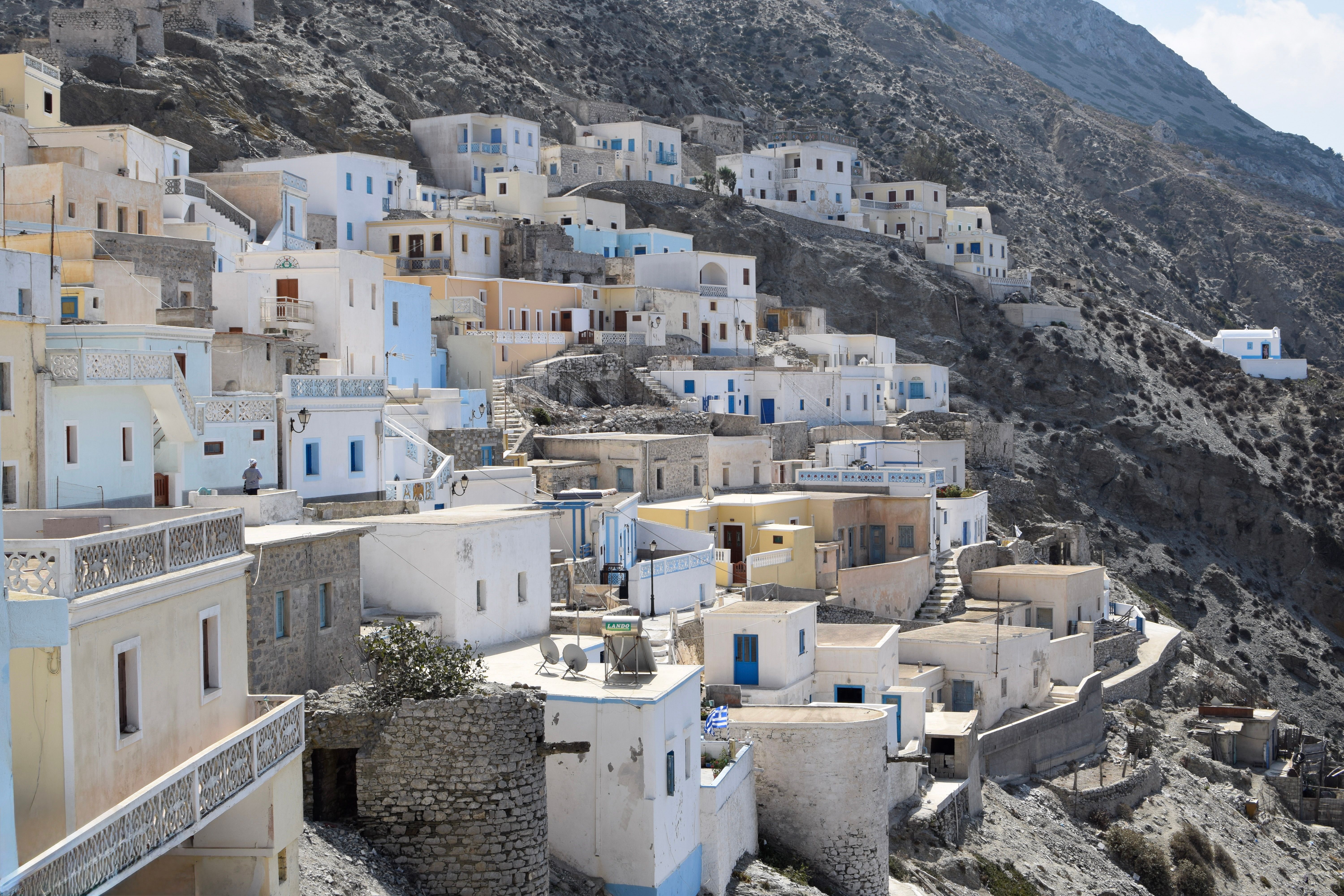 קרפתוס: Charming Greek island village with whitewashed houses nestled into a rocky hillside, under a bright sky.