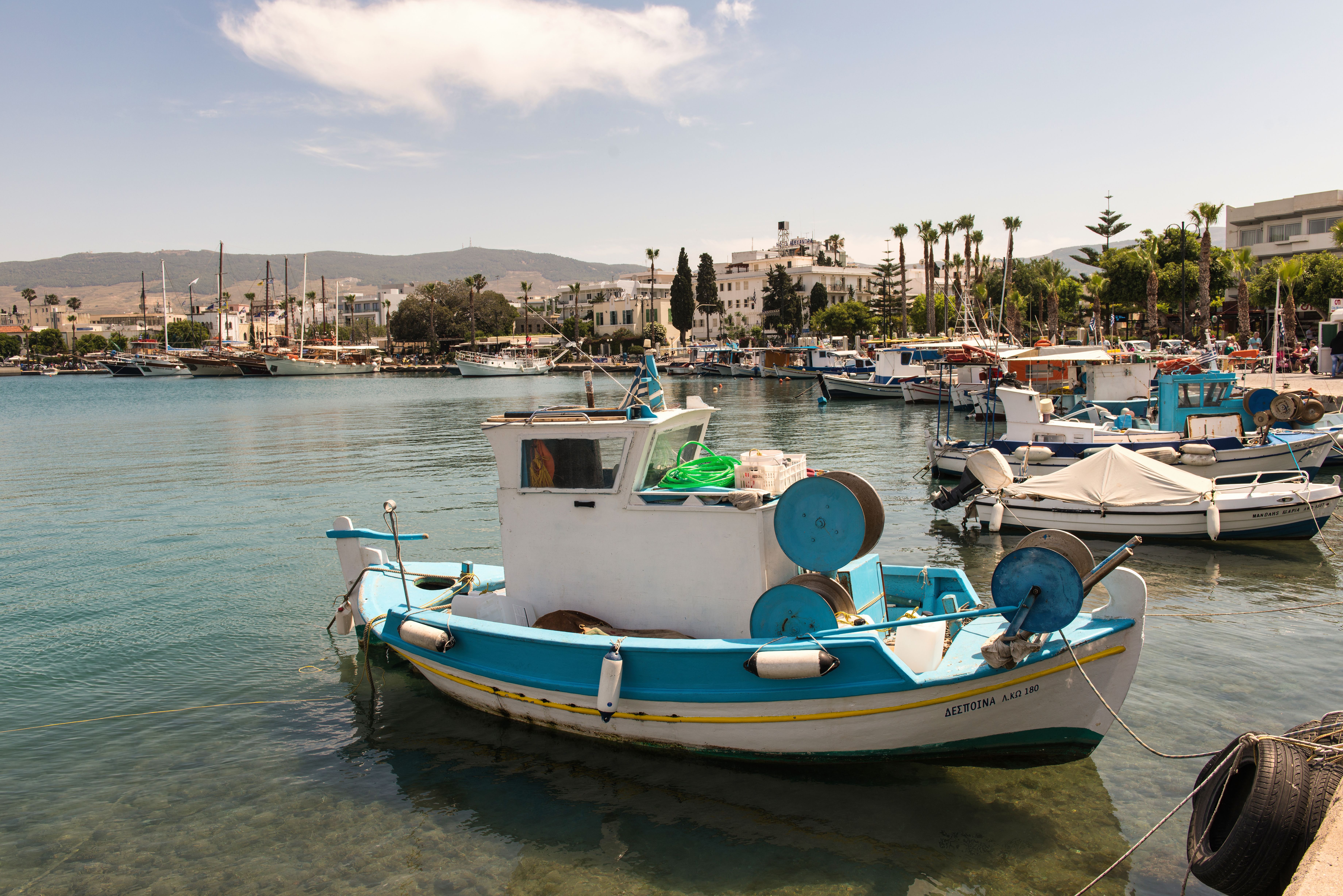 קוס: A serene view of fishing boats moored in the picturesque harbor of Kos, Greece, under a bright summer sky.