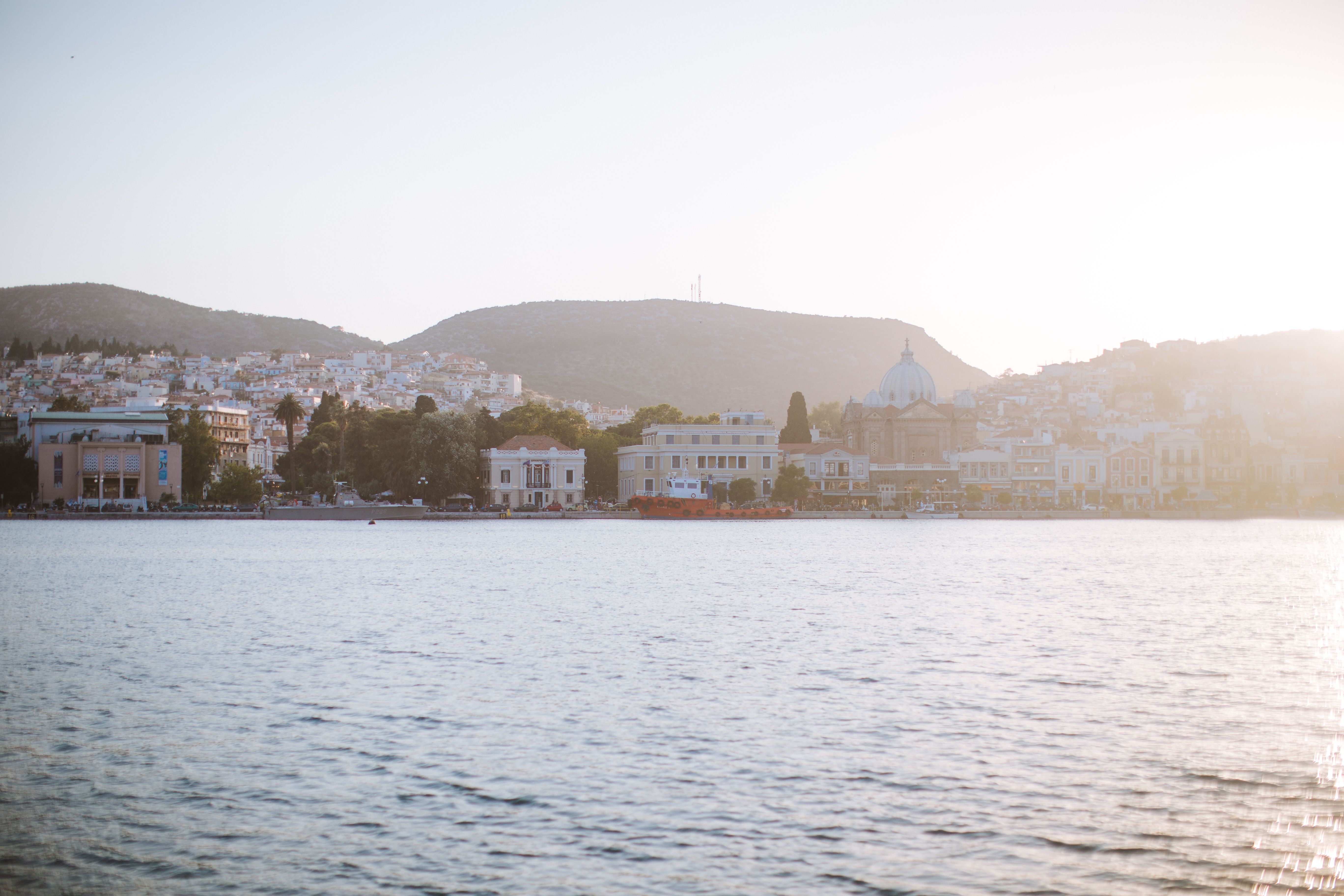 לסבוס: Beautiful coastal city scene with mountains and sea, capturing a soft sunset glow.